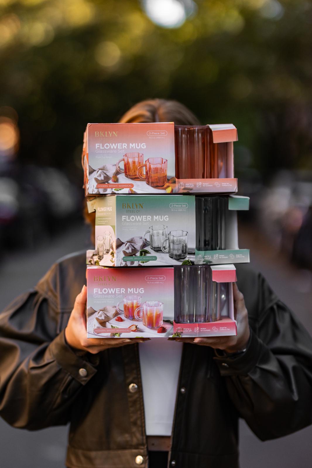 Person holding a stack of 'Flower Mug' product boxes with a blurred background